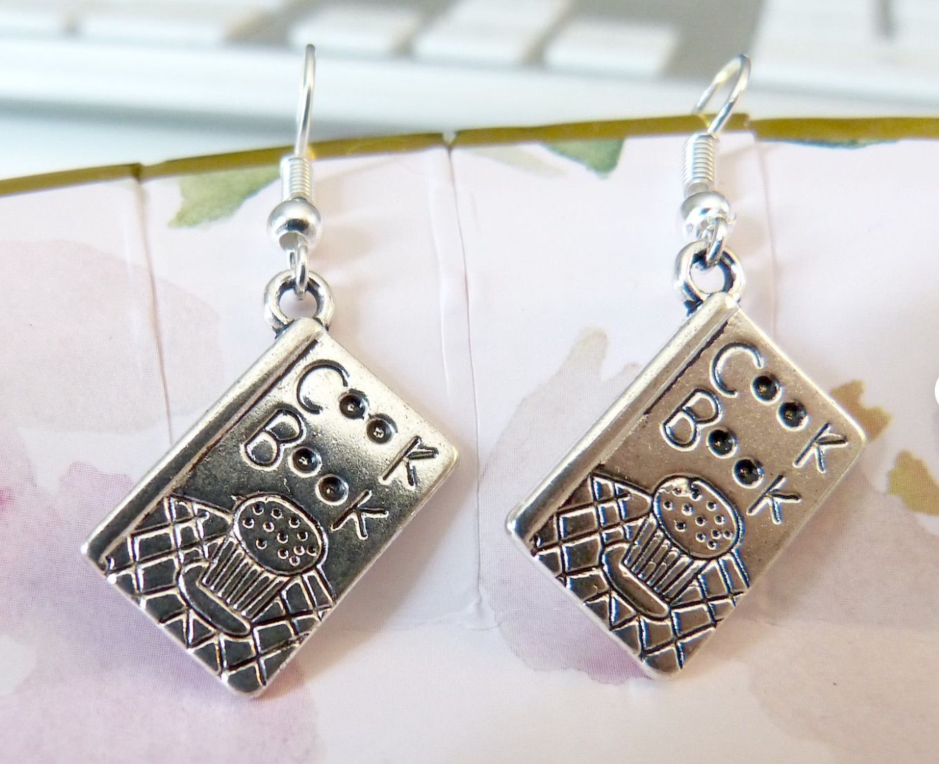 Silver earrings with cookbook charms.