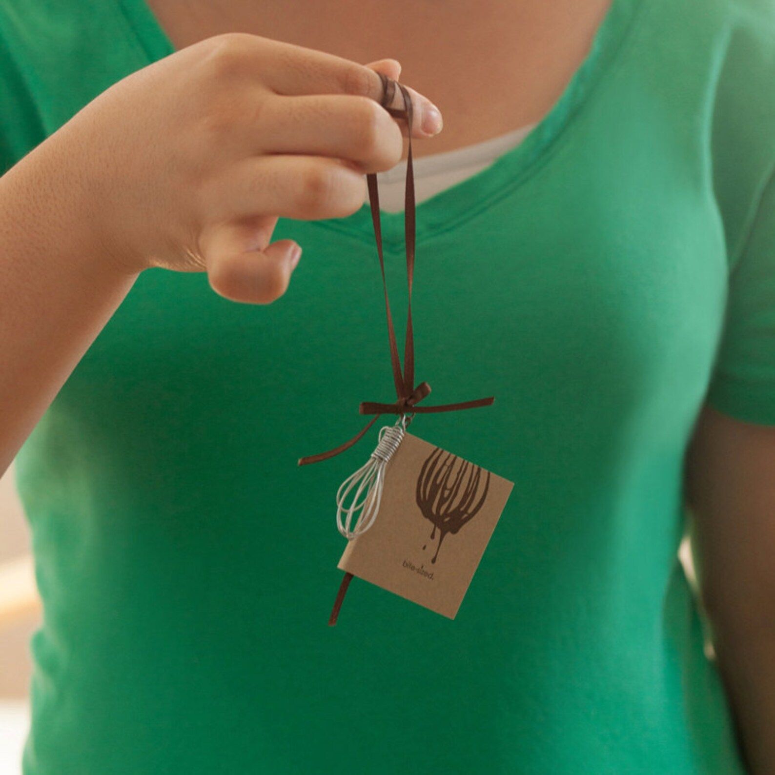 Image of a miniature cookbook and whisk with a brown string to hang them. 