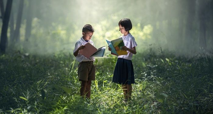 two children reading a book in a green wooded area