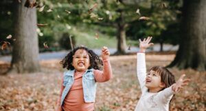 two laughing children tossing dried leaves in the air