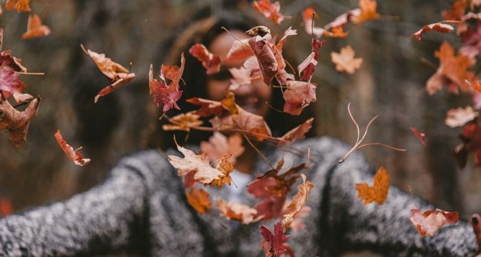 person throwing dried maple leaves in the air