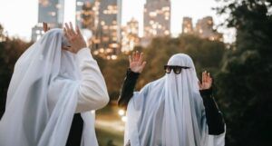 two people dressed as ghosts in white sheets with sunglasses high-fiving one another