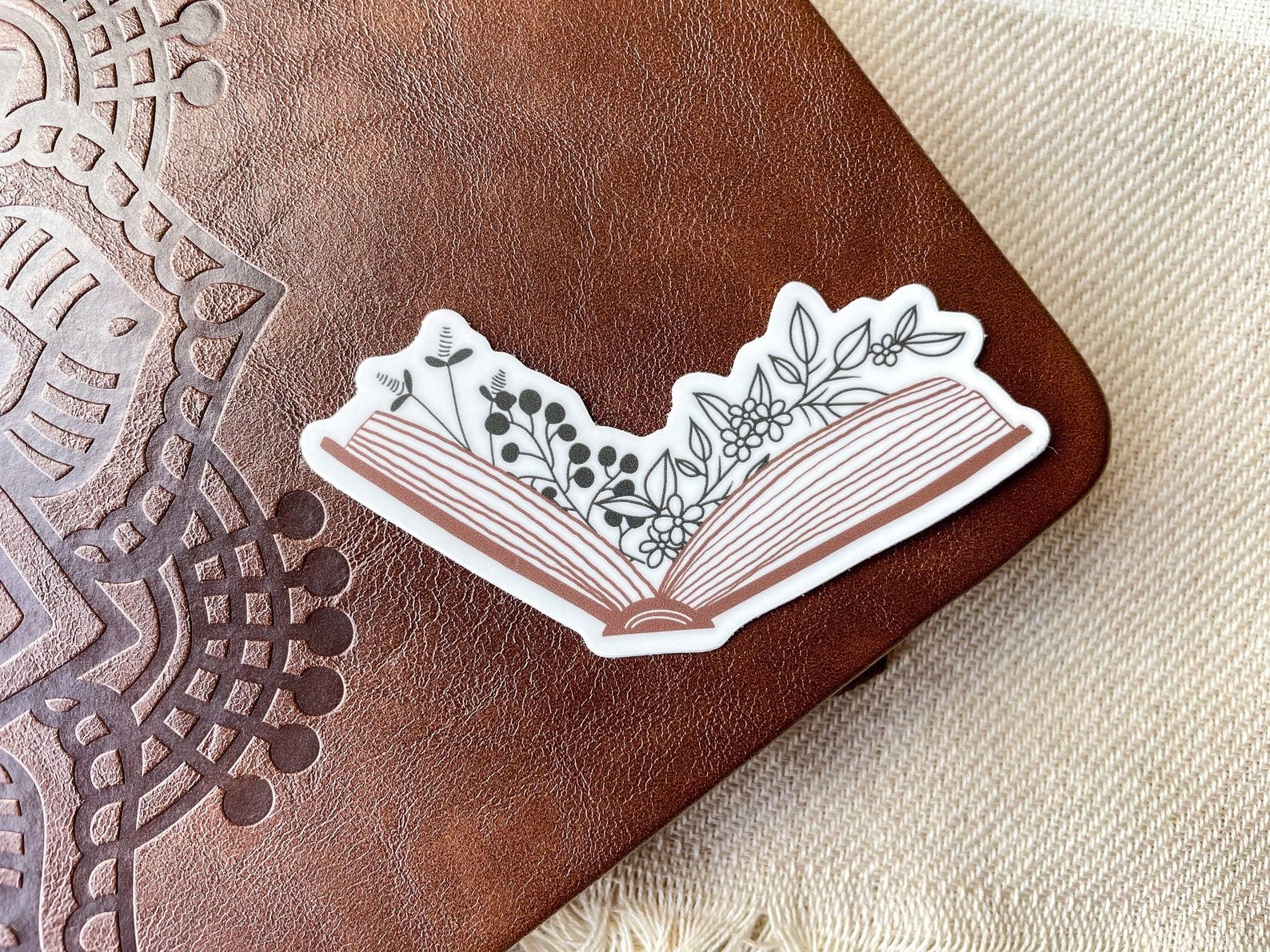 Image of a sticker featuring an open brown book with flowers coming from the pages. 