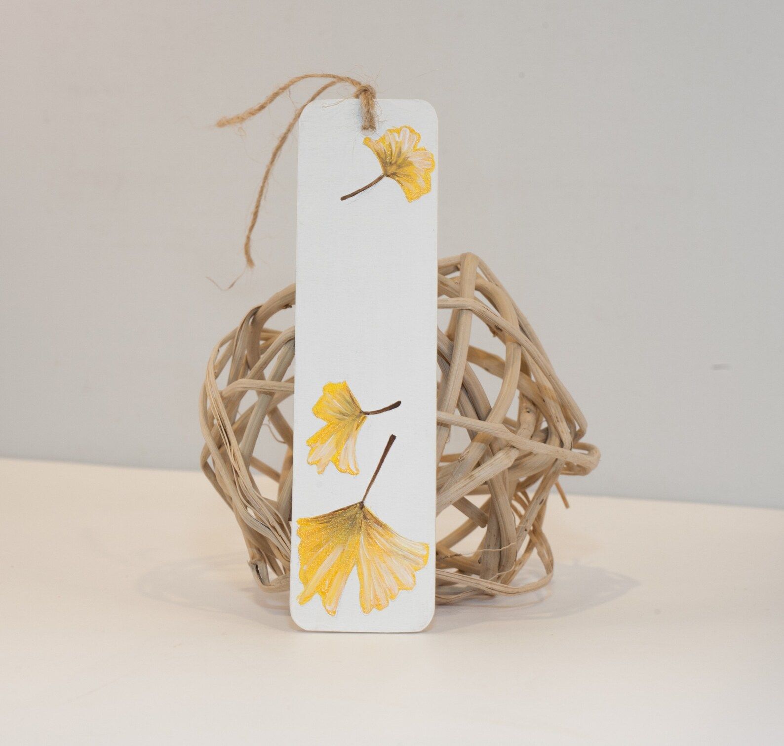 Image of a white bookmark with golden pressed ginko leaves. 