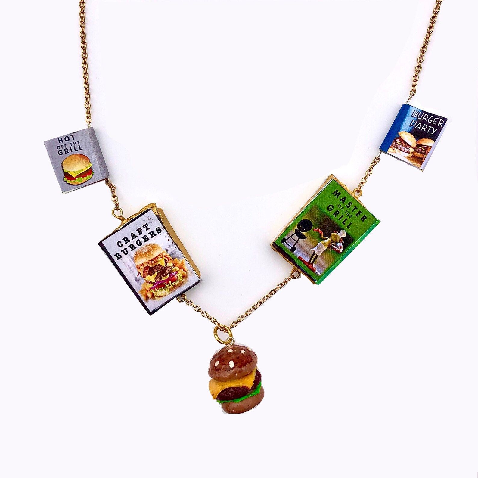 Image of a necklace with burger and grilling cookbook charms. There is a burger charm at the center. 