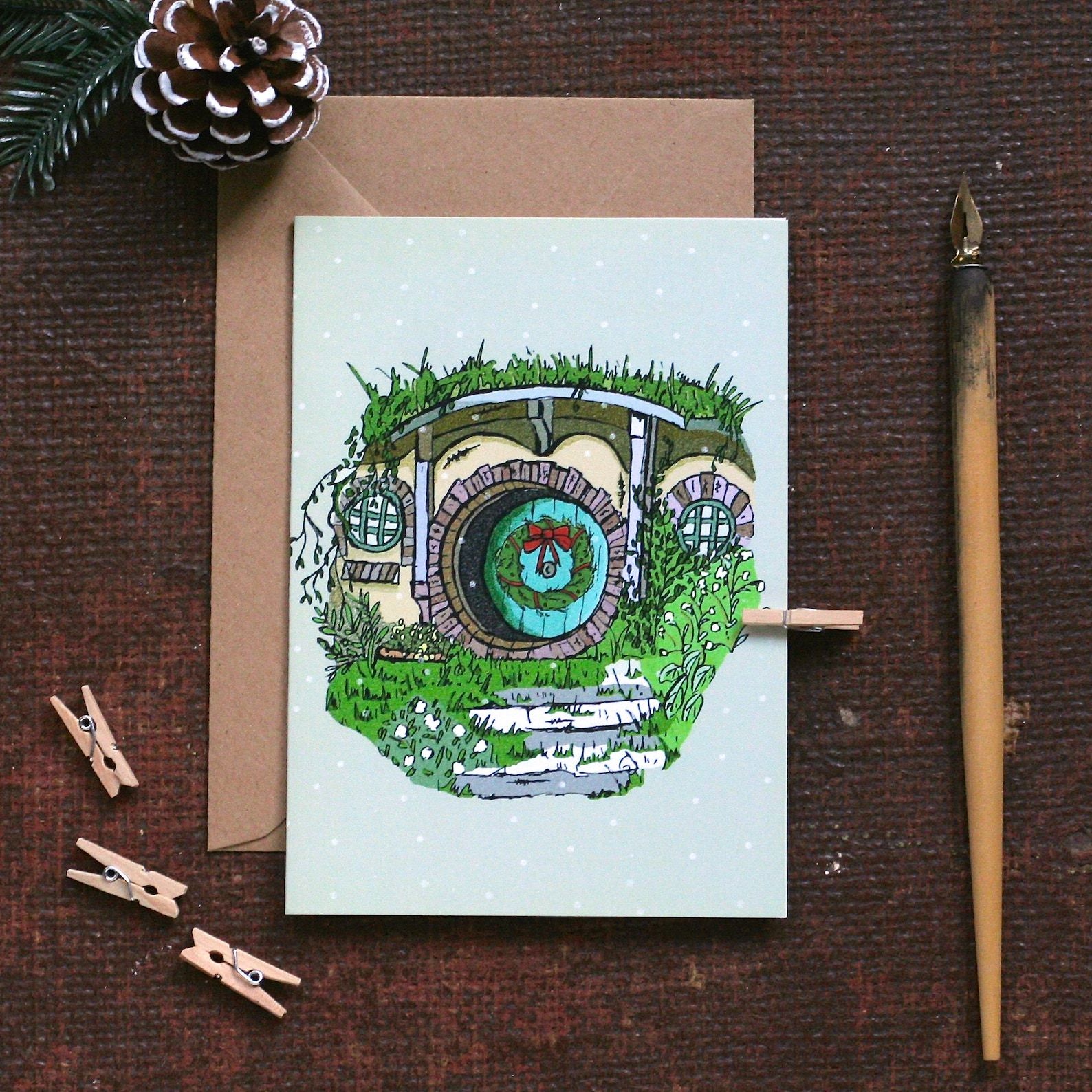 A painting of a Hobbit hole with a wreath on the door and snowflakes falling.