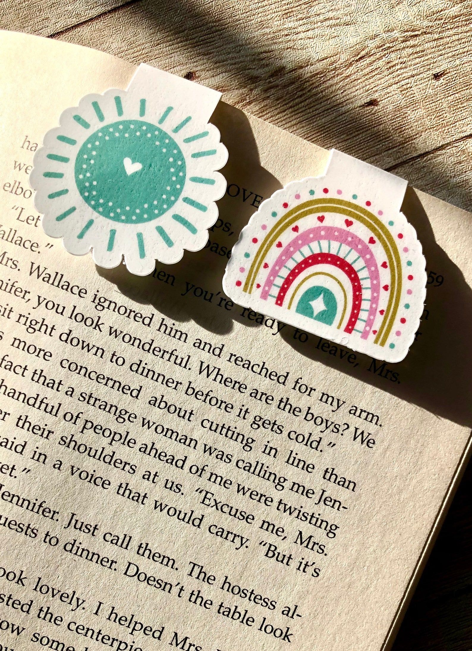 Two magnetic bookmarks on top of a page. The one on the left is a turquoise design, while the one on the right is a brightly colored rainbow. 