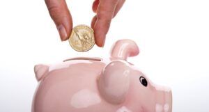a hand placing a gold coin into a pink piggy bank