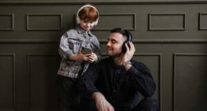 a child and adult both wearing headphones and looking at a mobile phone