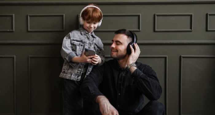 a child and adult both wearing headphones and looking at a mobile phone