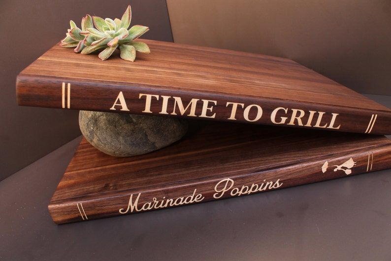 Two cutting boards designed like books. The top one is titled "A time to grill." The bottom one is titled "Marinade poppins."