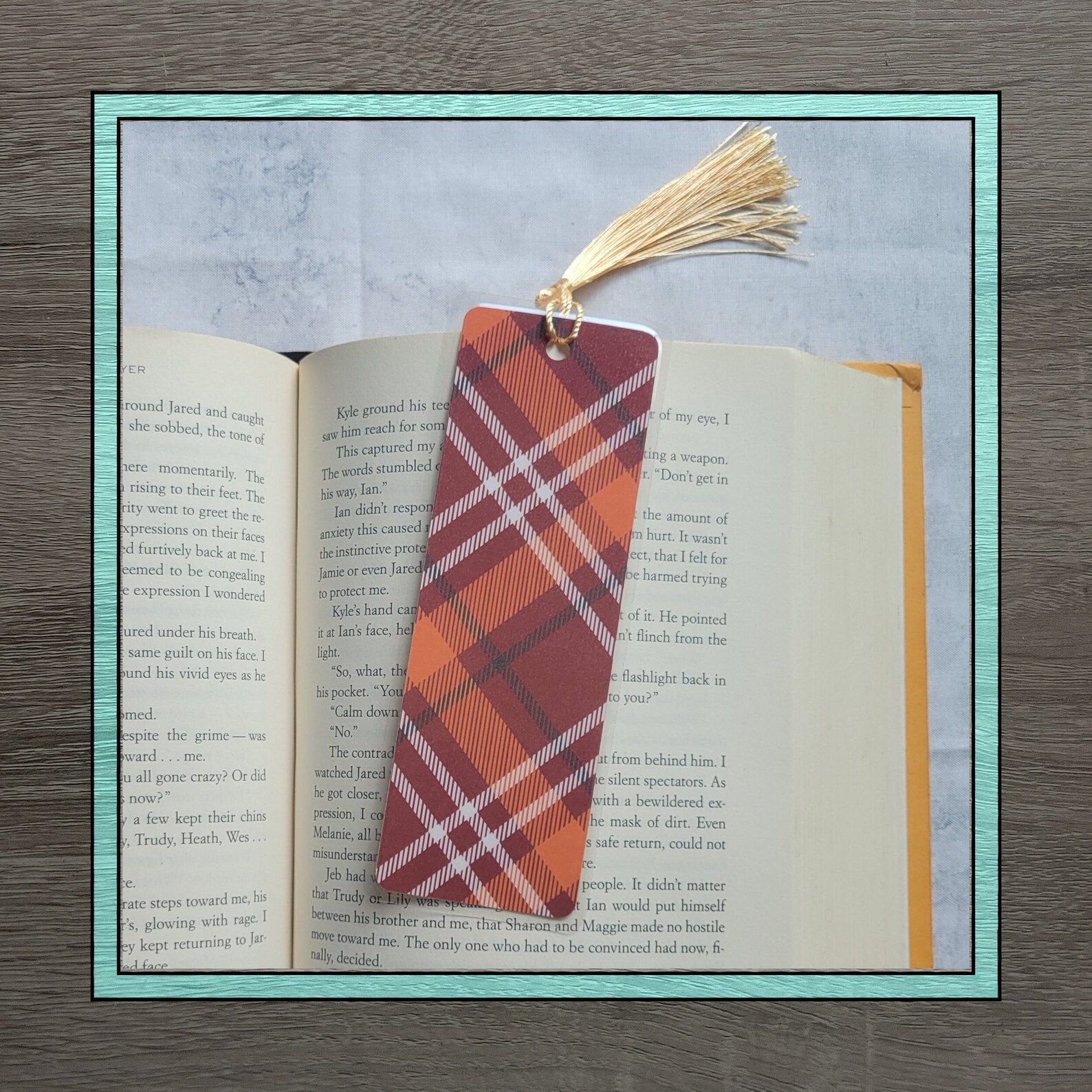 Image of a bookmark on an open book. The bookmark is orange, red, and white plaid. 