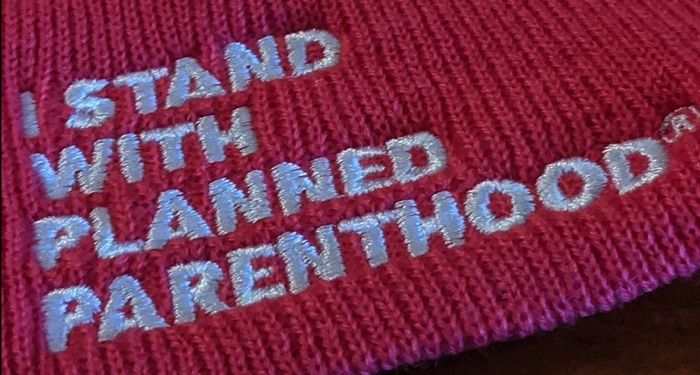 white embroidered text on a pink hat that says "I Stand with Planned Parenthood"