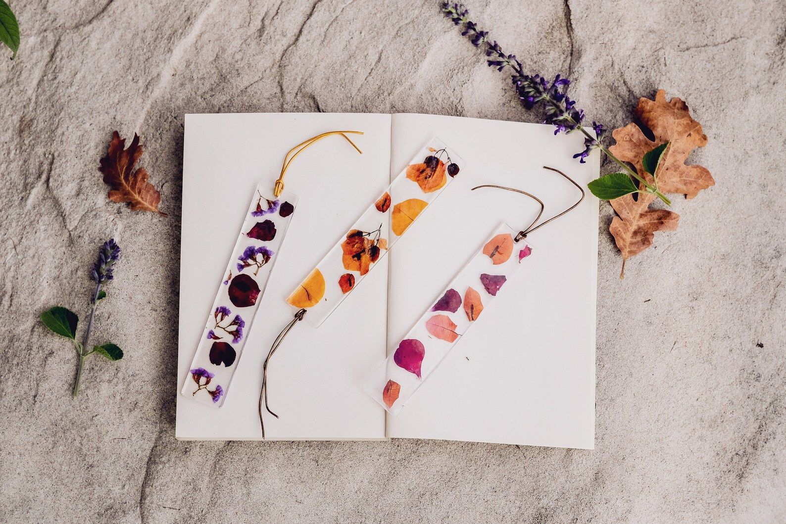 Image of three pressed flower bookmarks with tassels on an open blank book.