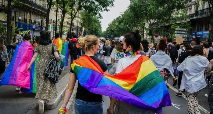 queer women holding hands with rainbow flag draped over both of them