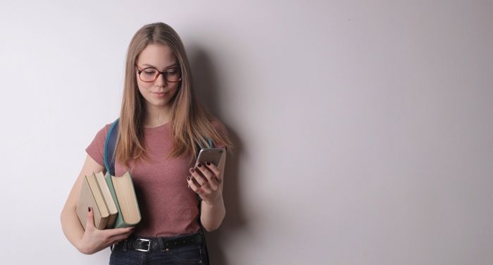 a woman holding a stack of books in one hand holding up a mobile phone in the other