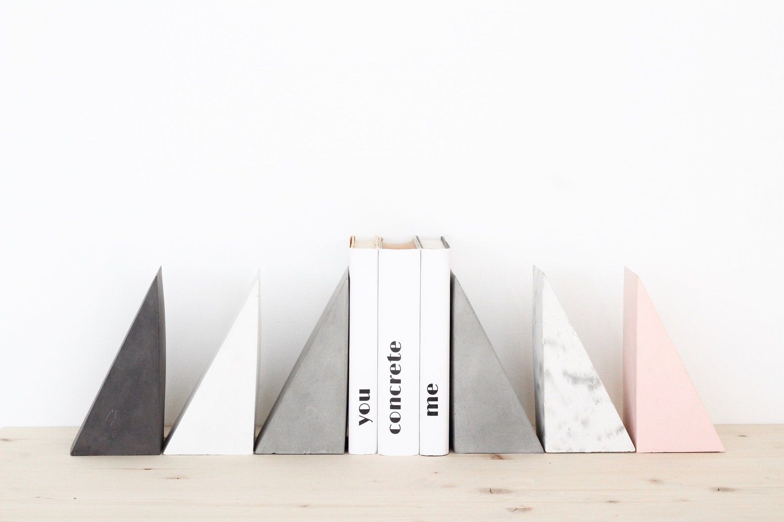 Several concrete triangle bookends in different colors—black, white, grey, and pink—sit on either side of a stack of books.
