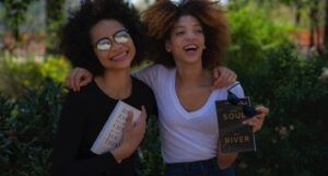 two women smiling, hugging, and holding books
