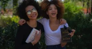 two women smiling, hugging, and holding books