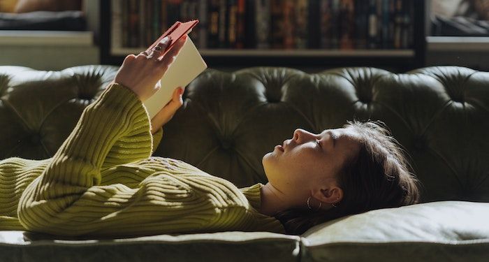 a photo of a woman lying on a couch reading