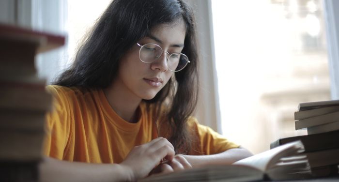 a woman reading a book with stacks of books piled to her left and right