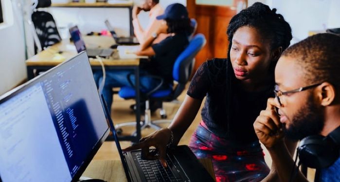 a Black woman showing a Black man something on a laptop in a classroom