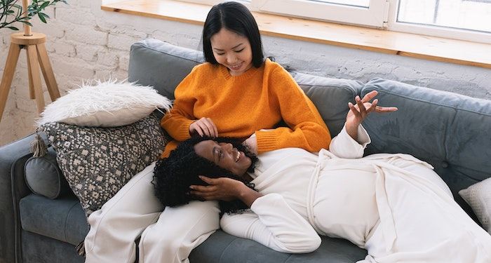 Black and Asian woman cuddling on couch and smiling