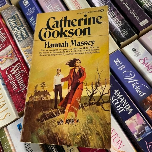 la couverture d'un livre intitulé Hannah Massey, avec une femme courant d'un manoir dans un paysage sombre avec un manteau rouge drapé sur une épaule