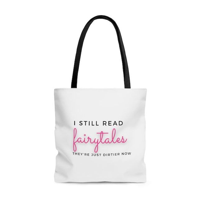 A white polyester shoulder tote that says "I still read fairytales they're just dirtier now" in black and pink letters 
