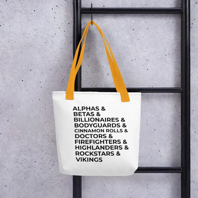 A white polyester shoulder back with yellow straps and black writing that says: 
Alphas & Betas & Billionaires & Bodyguards & Cinnamon Rolls & Doctors & Firefighters & Highlanders & Rockstars & Vikings