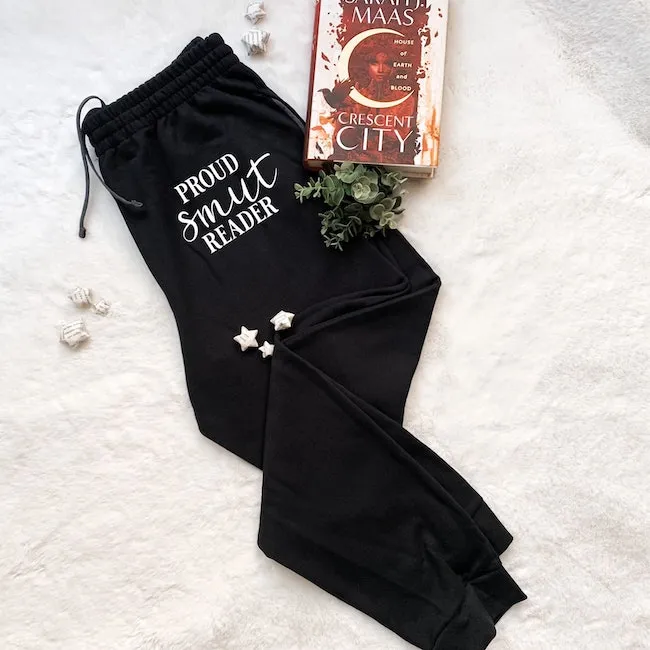 Black pants on a which background. The pants have white writing on them that say, "Proud Smut Reader."