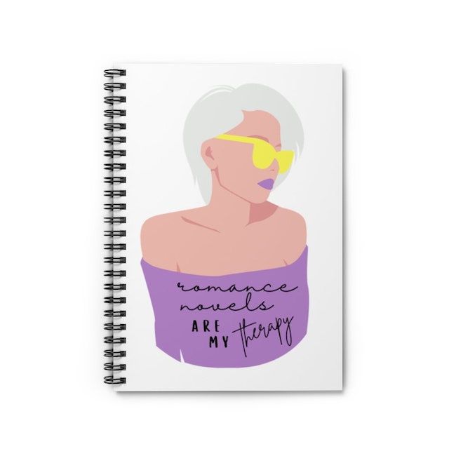 A white spiral notebook with a stylized white woman on the front. She is wearing yellow sunglasses, rocks a grey pixie shag haircut, and is wearing an off-shoulder purple shirt that says "romance novels are my therapy." 