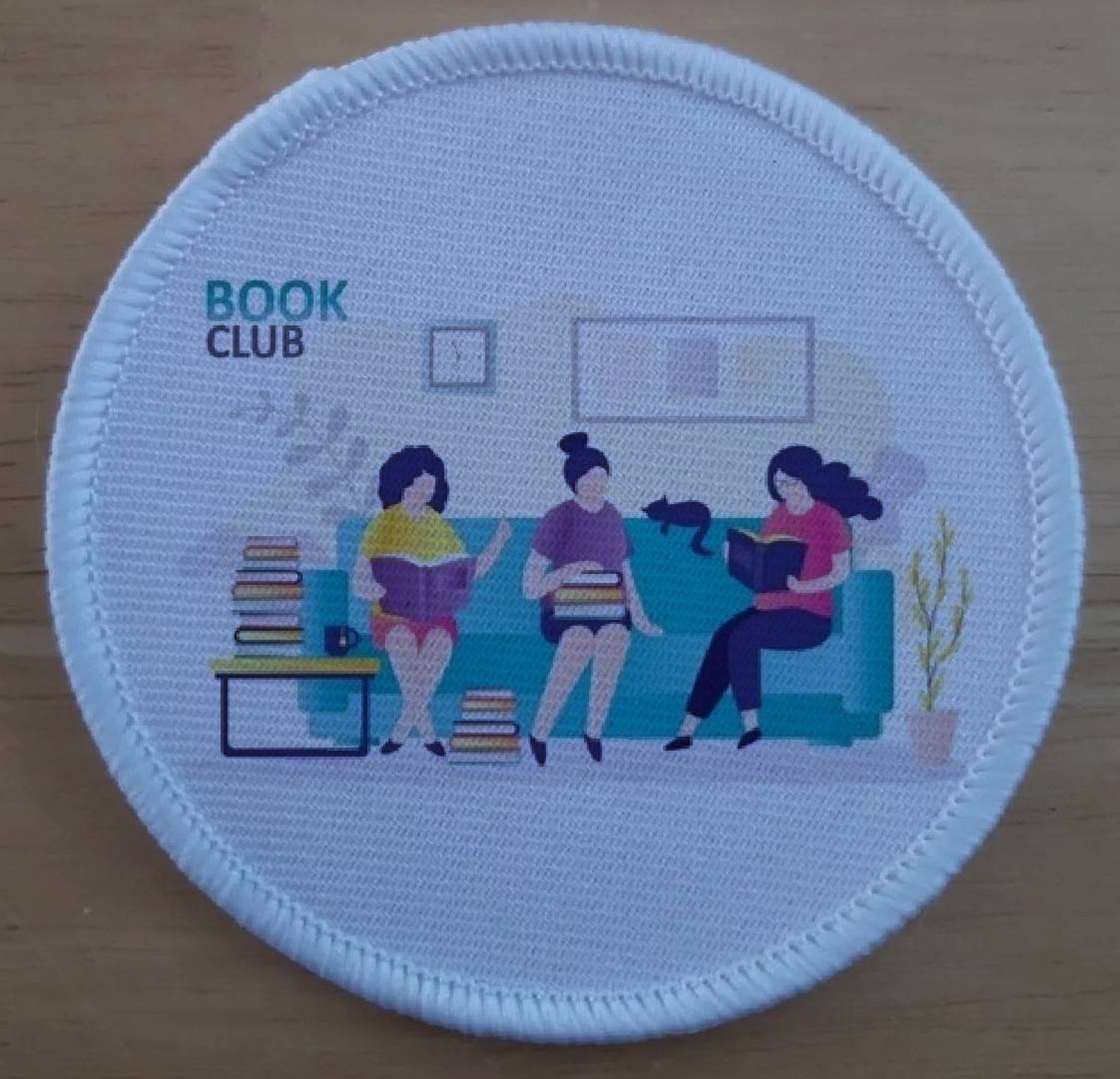 écusson à coudre montrant trois femmes lisant sur un canapé, avec un chat, et les mots Book Club sur le mur. 