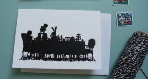 A greeting card with a black silhouette of the characters from Alice in Wonderland at a tea party,