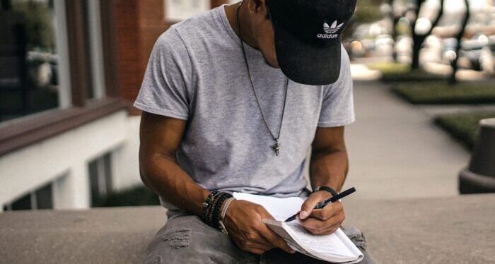 person in black adidas cap sitting on bench writing on notebook