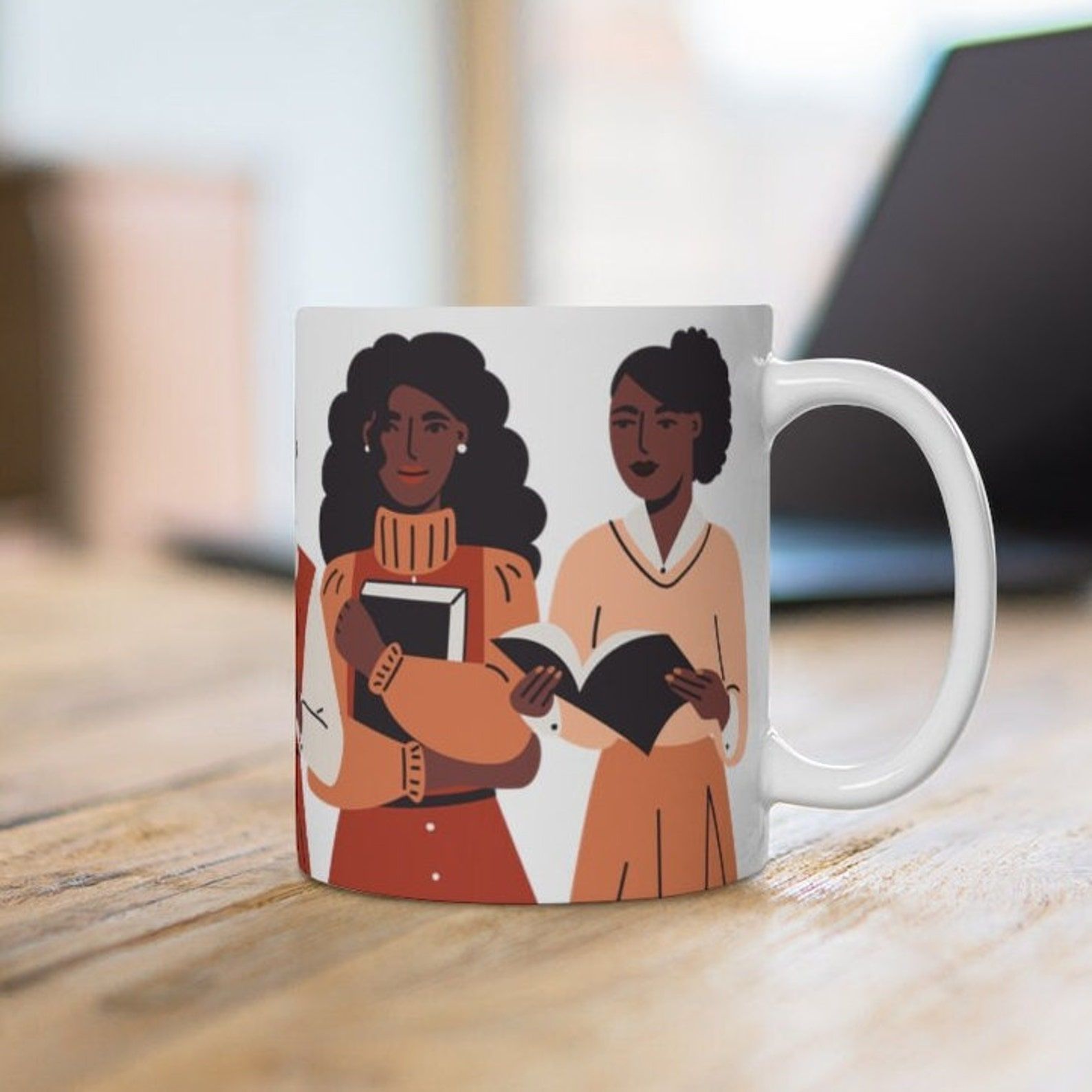 A while mug featuring three Black women in dressed in orange, tan, and cream, each holding a book.