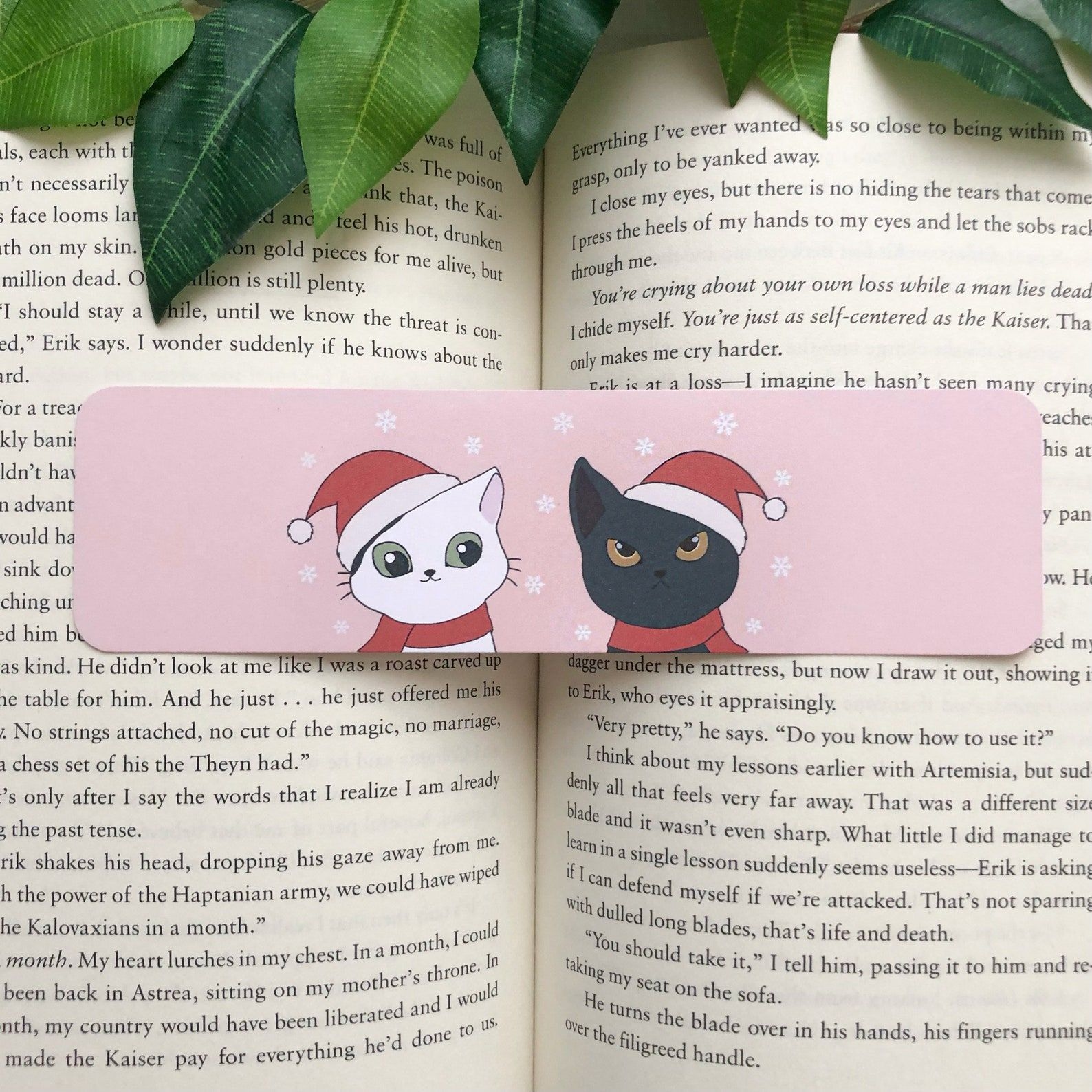Image of a pink bookmark with a white and black cat. Both are wearing santa hats and red scarves. 