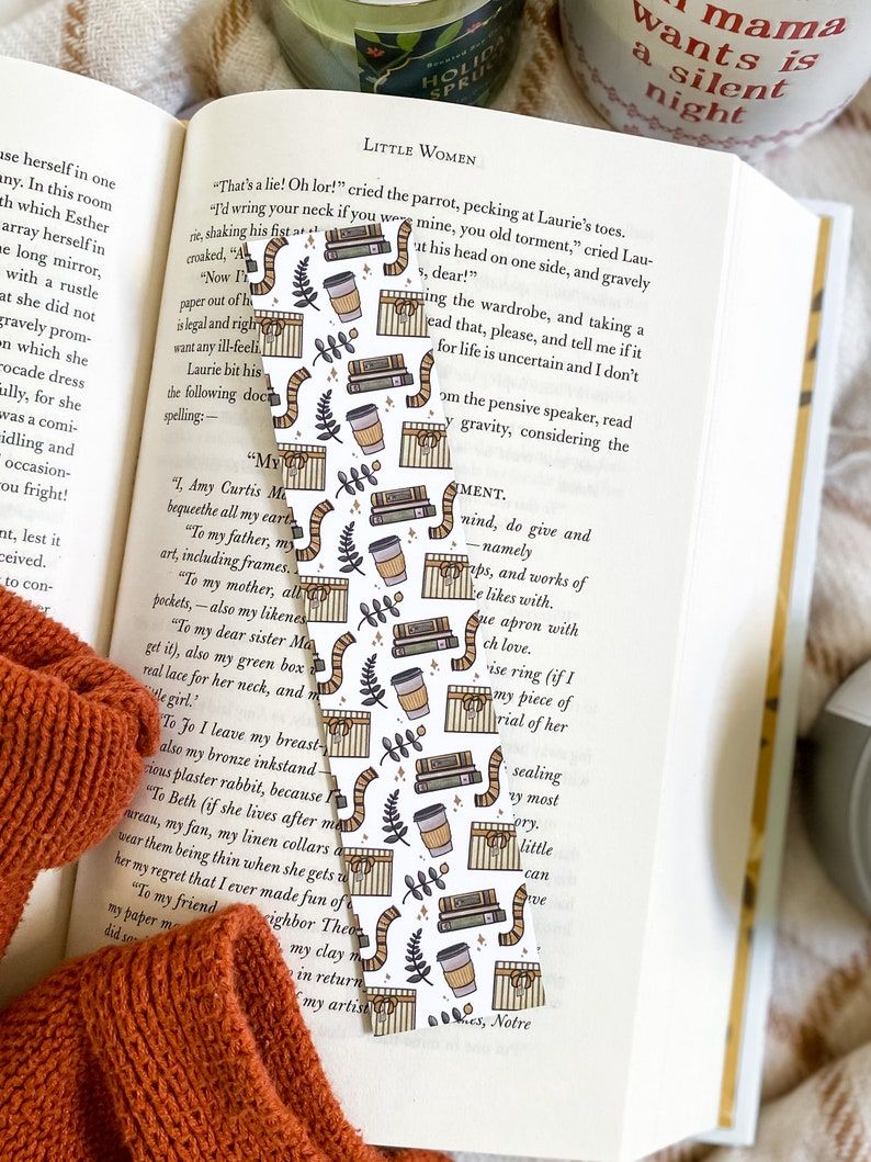 Image of a white bookmark on an open book. The bookmark features a pattern of coffee, leaves, scarves, and books in a winter color scheme. 
