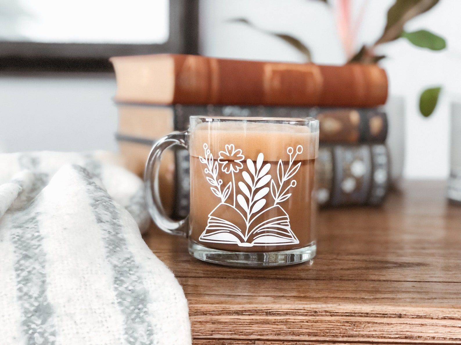 Tasse en verre sur une table.  La tasse a un livre blanc avec des fleurs qui poussent sur les pages. 