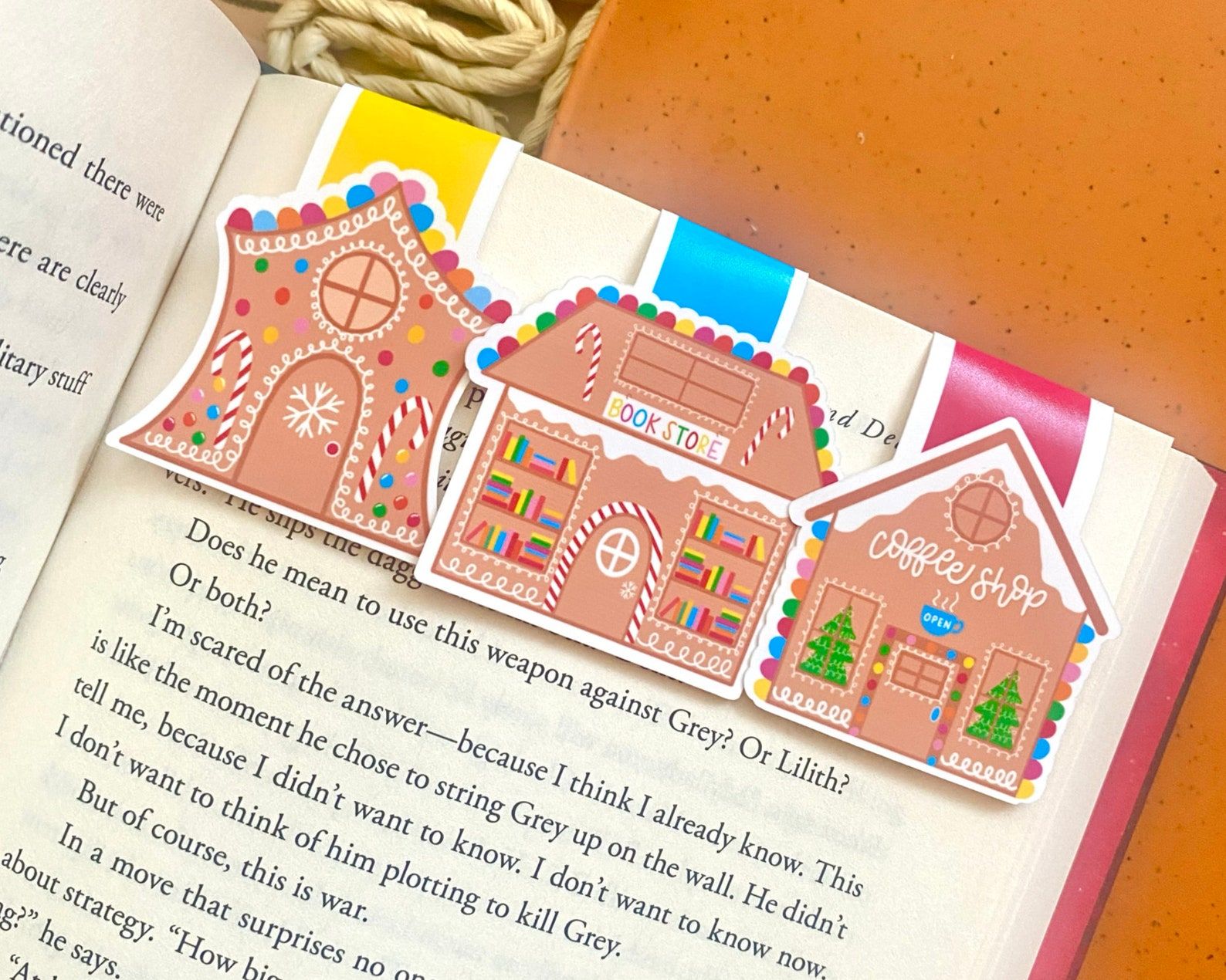 Three magnetic bookmarks in the shape of gingerbread houses in a row at the top of a book page. 