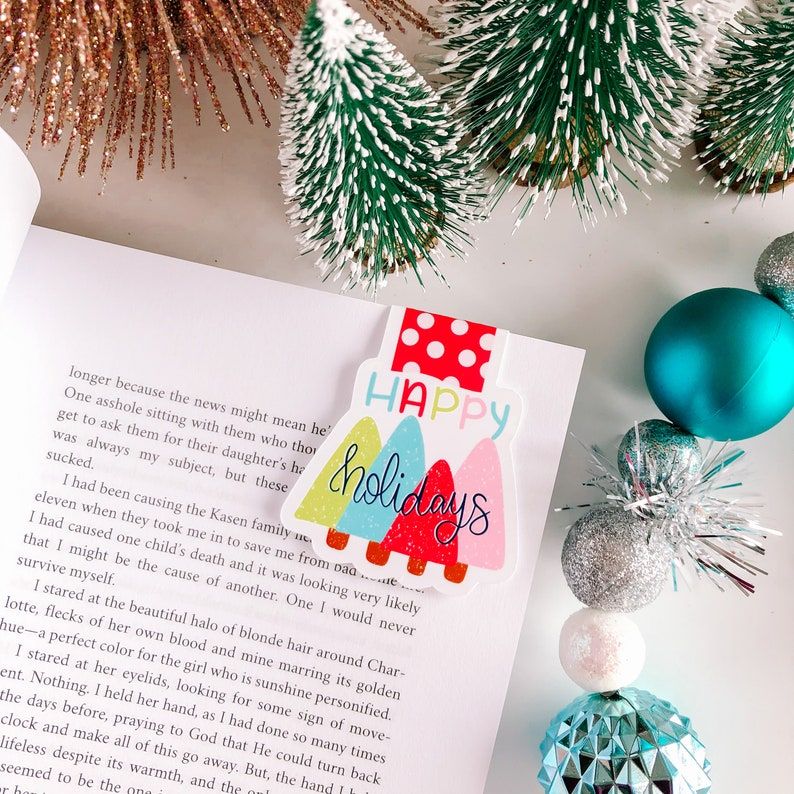 Magnetic bookmark in red, blue, green, and pink. It redas "happy holidays" with a series of Christmas trees. 