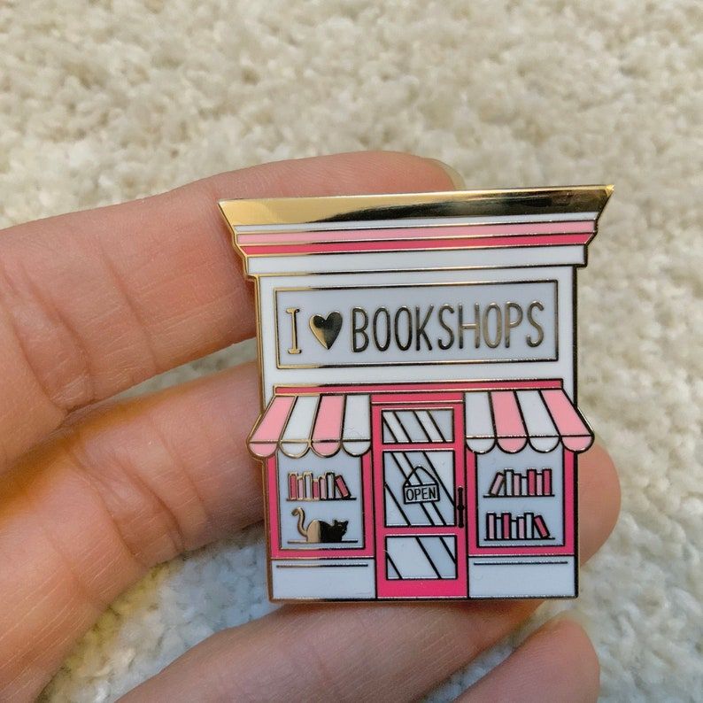 Image of an enamel pin. It's a pink bookshop store front, with the words 