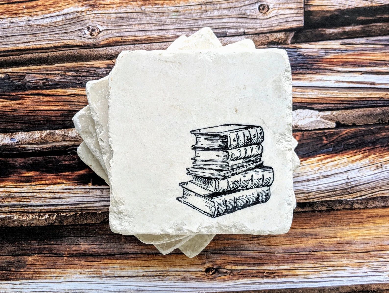 White stone coasters decorated with six books drawn in black.