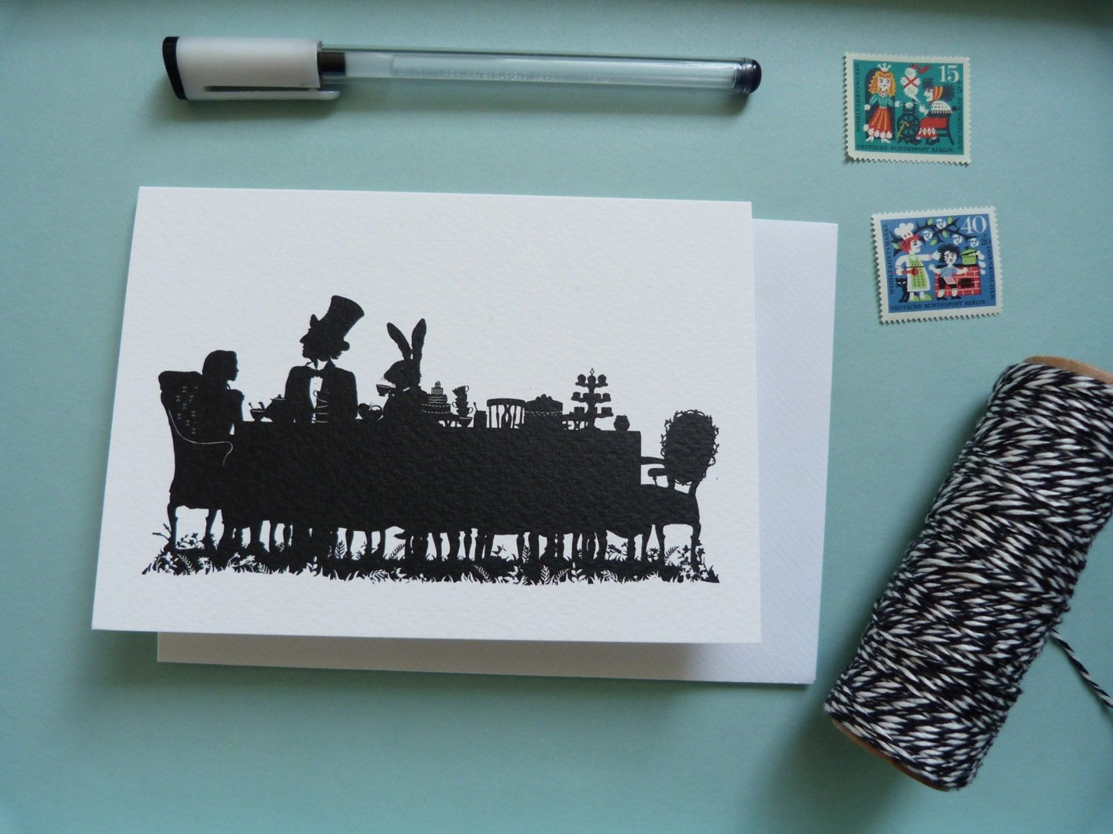 A greeting card with a black silhouette of the characters from Alice in Wonderland at a tea party,