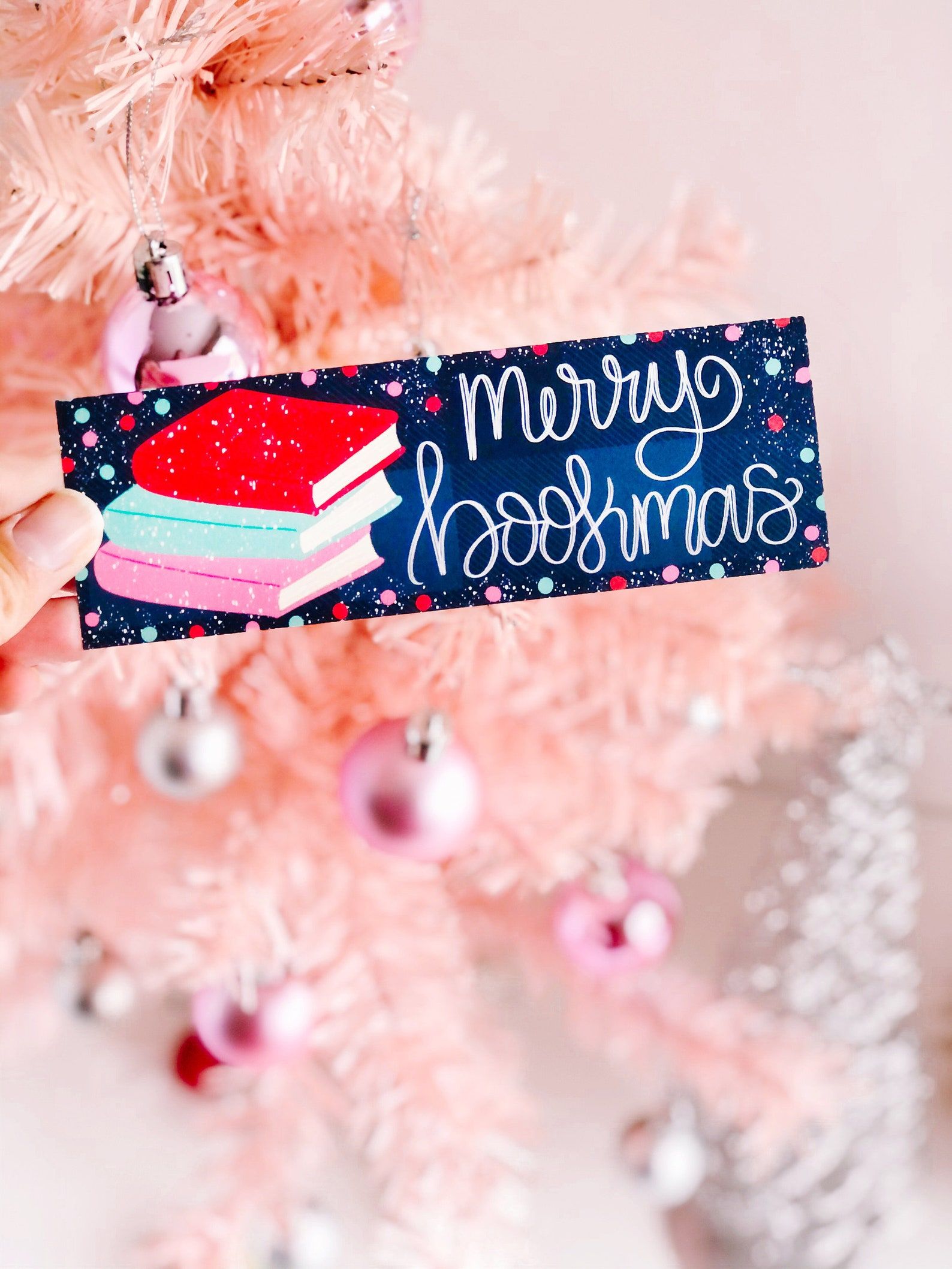 Image of a bookmark reading "merry bookmas" in front of a light pink Christmas tree. 
