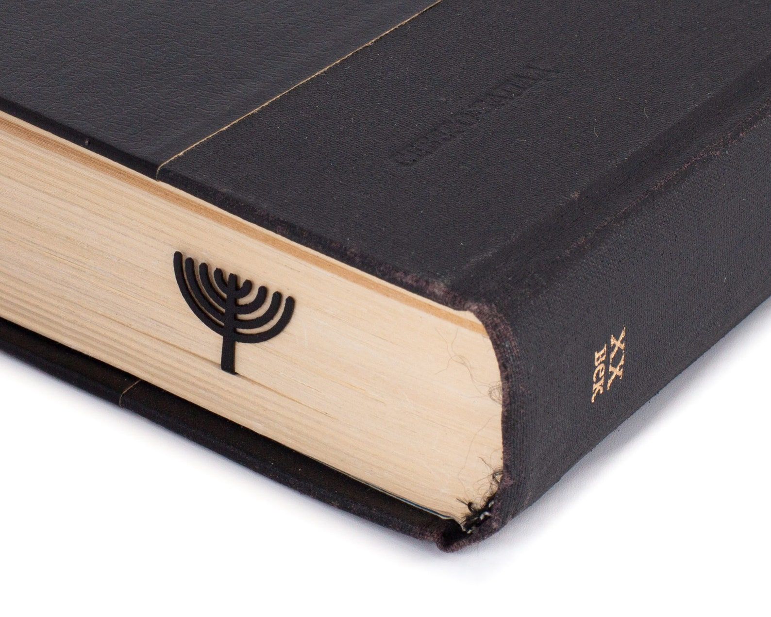 Image of a black metal menorah bookmark on the outside of the pages of a closed book. 