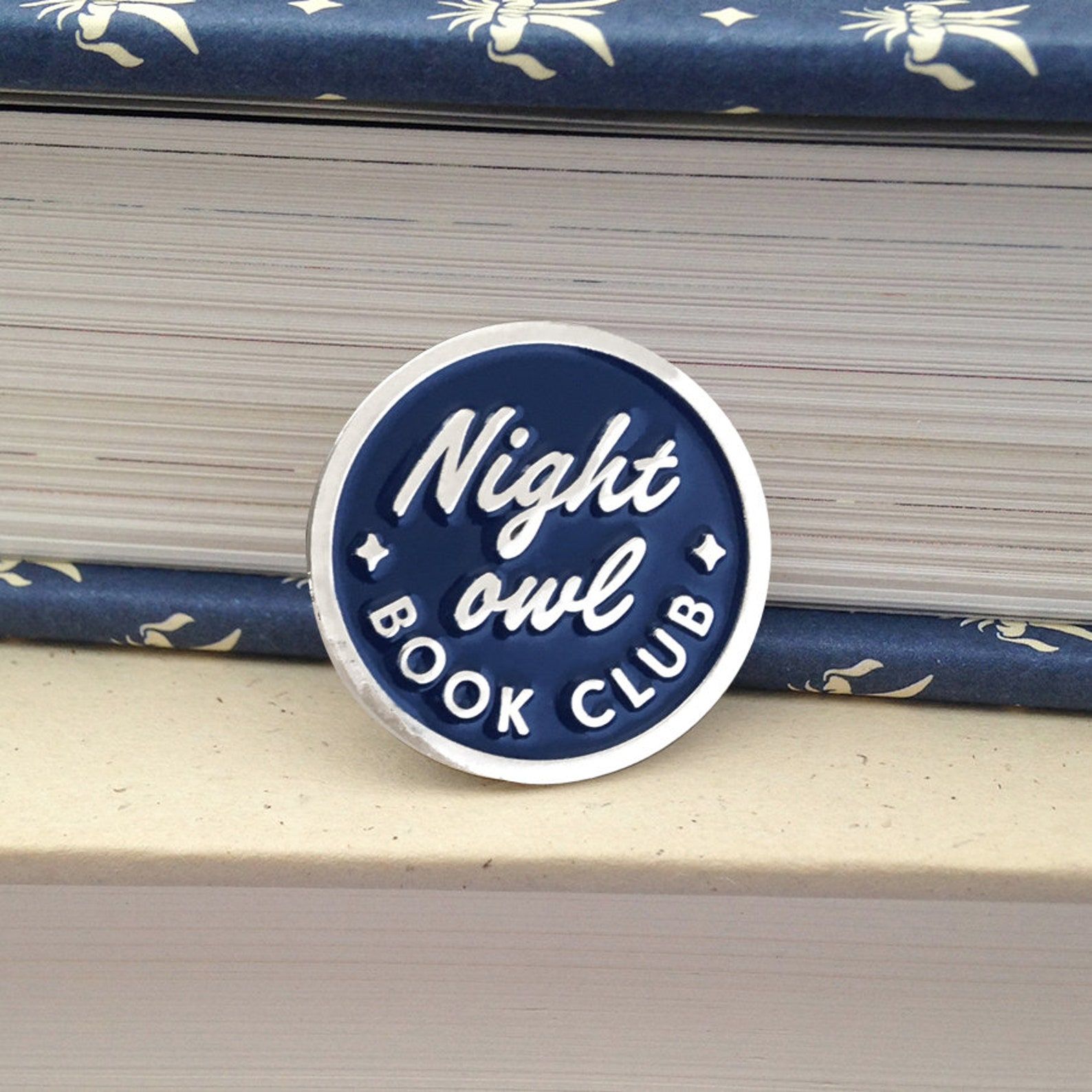 A round blue and solver enamel pin that reads "Night owl book club"