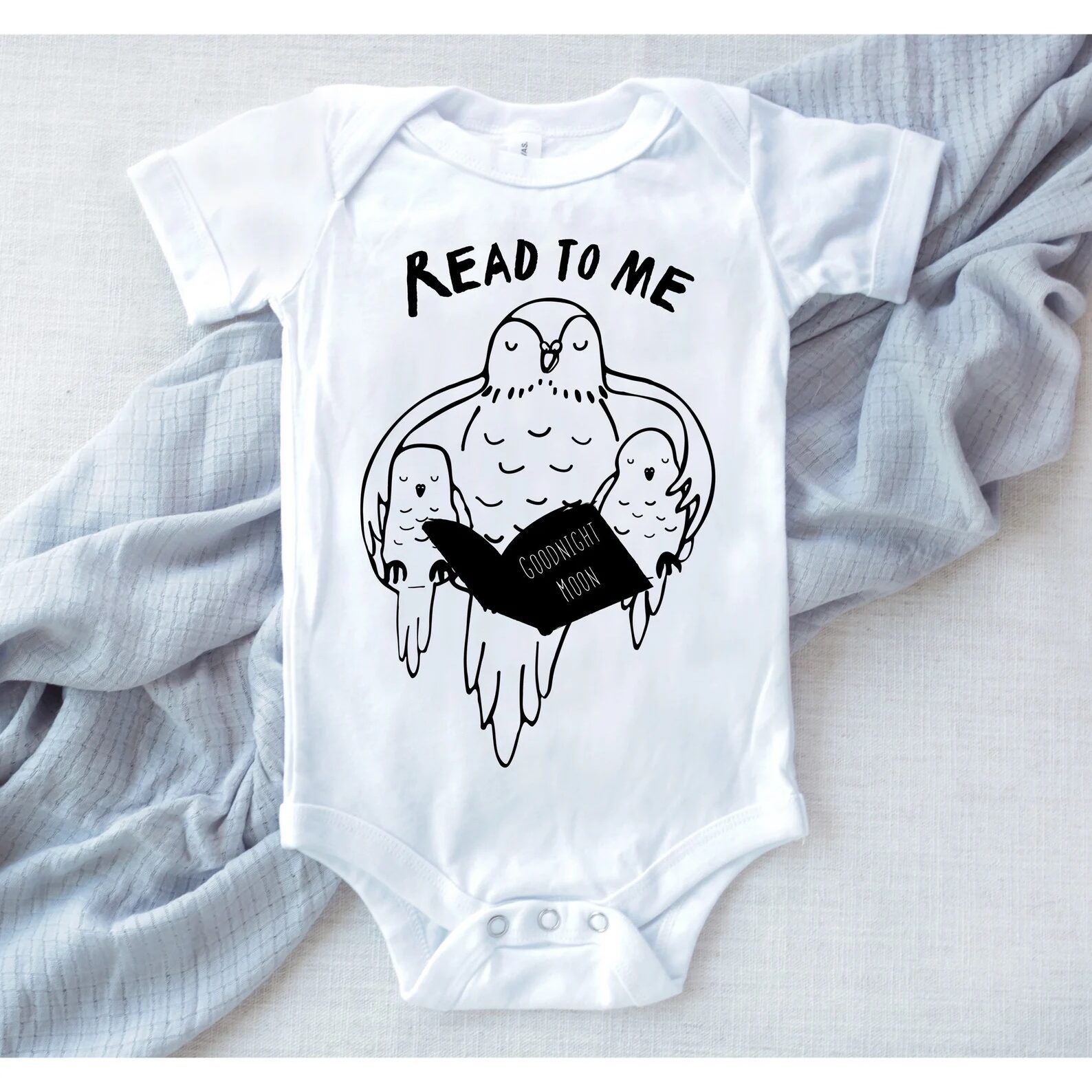White baby onesie with the words "read to me" and an adult owl reading to two baby owls.