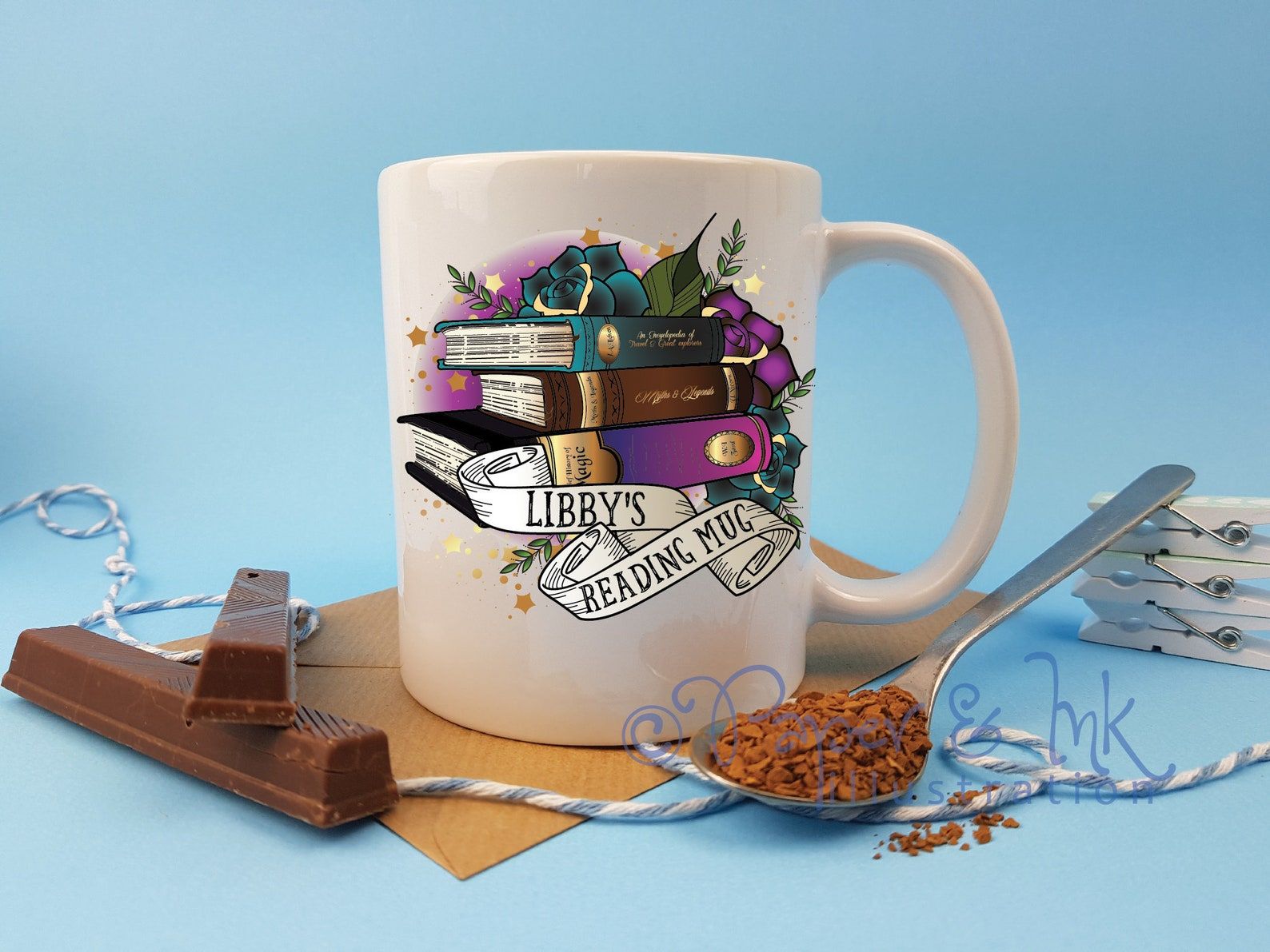 Image of a white mug behind chocolate sticks. The mug has colorful books, with text that can be customized. It reads "Libby's Reading Mug." 