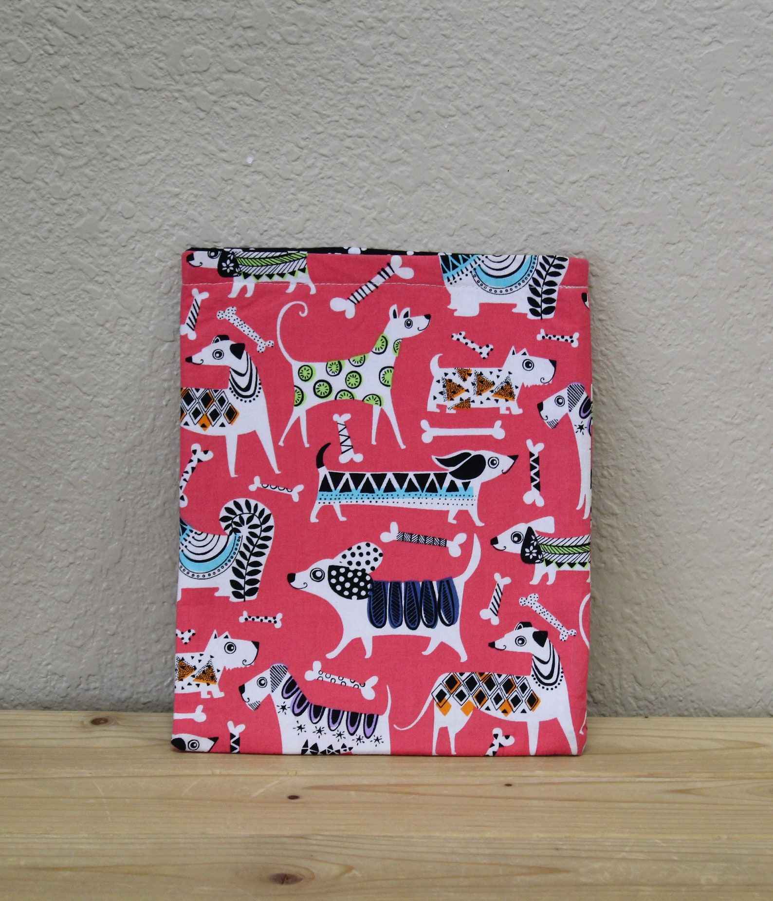 A book sleeve made out of a pink fabric with colorful dogs on it. 
